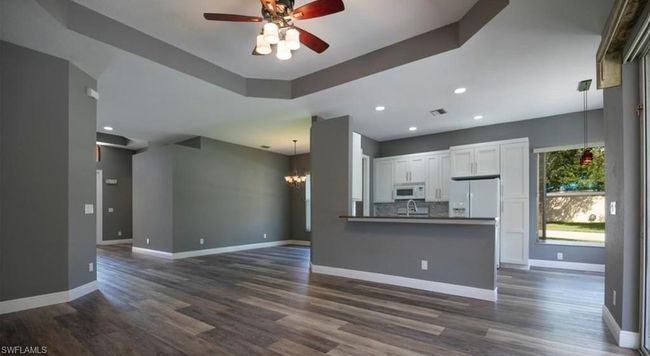 Unfurnished living room featuring dark hardwood / wood-style floors, ceiling fan with notable chandelier, and a raised ceiling | Image 6