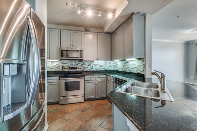 Kitchen with double stainless steel sink, stainless steel appliances, gray cabinetry, decorative backsplash, and dark granite countertops | Image 16