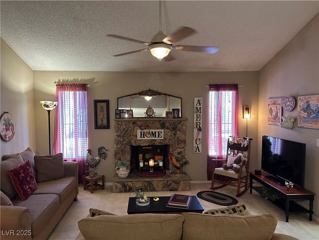 Carpeted living room featuring ceiling fan, a stone fireplace, and a textured ceiling | Image 8