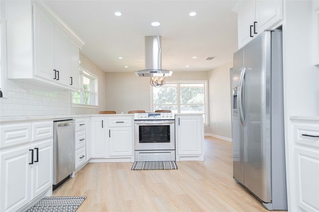 Kitchen with appliances with stainless steel finishes, a peninsula, island range hood, light wood-style flooring, and light countertops | Image 13