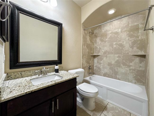 This bathroom features a modern design with a granite countertop, dark wood vanity, and a large framed mirror. It includes a bathtub with a tiled shower area and recessed lighting for a clean, elegant look. | Image 44