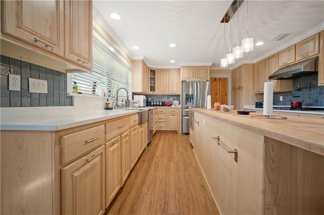 Kitchen with stainless steel fridge, light wood-type flooring, light brown cabinetry, under cabinet range hood, and a sink | Image 8