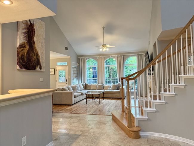 Living room featuring stone finish floor, ceiling fan, stairway, baseboards, and high vaulted ceiling | Image 17