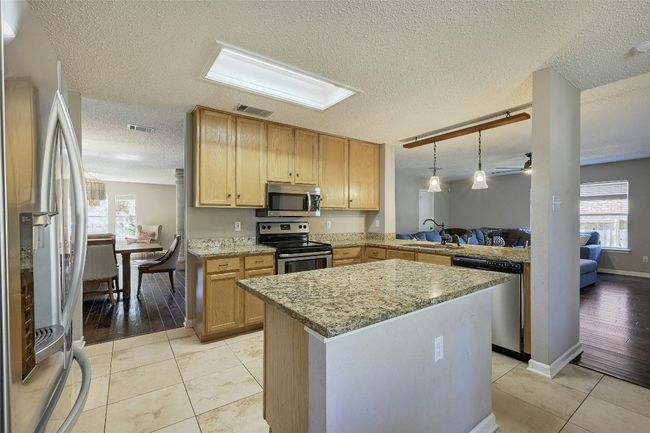 Kitchen with appliances with stainless steel finishes, a textured ceiling, light stone counters, a kitchen island, and pendant lighting | Image 11
