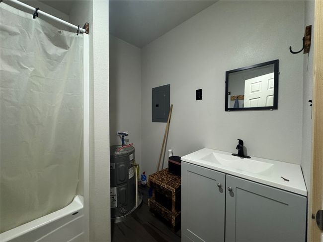 Bathroom featuring vanity, electric water heater, shower / bath combo with shower curtain, electric panel, and wood finished floors | Image 12