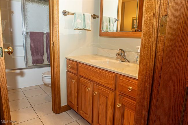 Full bathroom featuring tile patterned floors, bath / shower combo with glass door, toilet, and vanity | Image 18