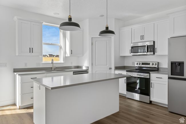Kitchen with appliances with stainless steel finishes, wood finished floors, white cabinetry, and a sink | Image 4