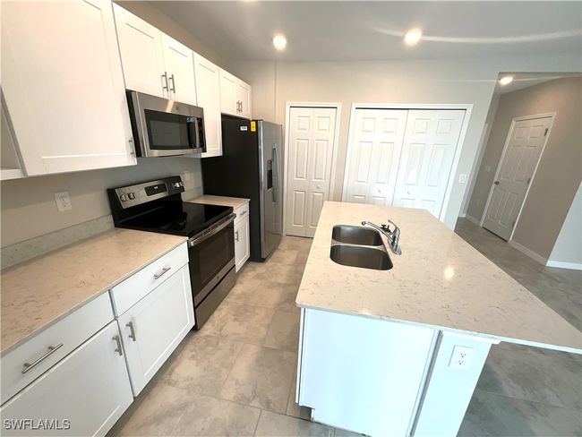 Kitchen with appliances with stainless steel finishes, a center island with sink, white cabinetry, and light stone counters | Image 4