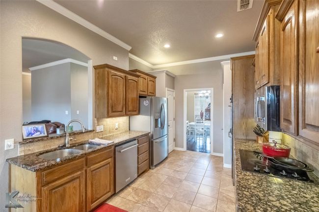Kitchen with stainless steel appliances, a sink, tasteful backsplash, dark stone counters, and brown cabinets | Image 9