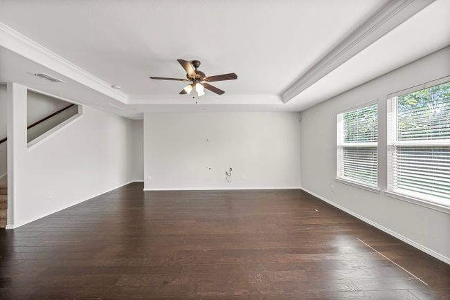 Spare room with a raised ceiling, a ceiling fan, dark wood finished floors, stairway, and crown molding | Image 10