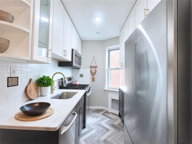 Kitchen featuring stainless steel appliances, decorative backsplash, white cabinets, and light stone countertops | Image 4