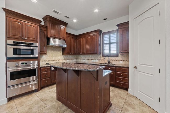 Kitchen with under cabinet range hood, a warming drawer, light tile patterned flooring, dark stone countertops, and recessed lighting | Image 15