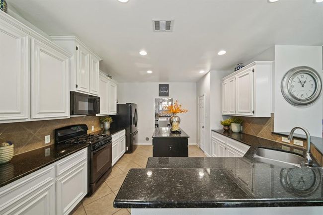White cabinetry, granite countertops, and tile flooring create a crisp, clean aesthetic, complemented by recessed lighting and a classic backsplash. | Image 21