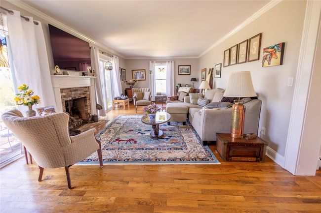 Living area with crown molding, a brick fireplace, wood finished floors, and baseboards | Image 6