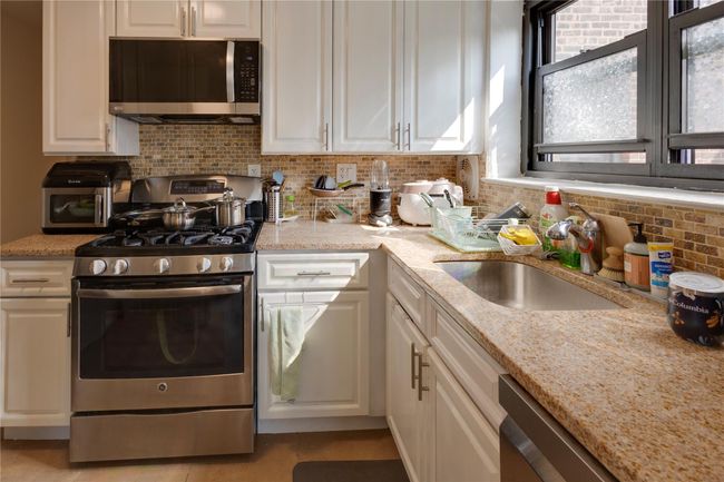 Kitchen featuring stainless steel appliances, a sink, white cabinetry, tasteful backsplash, and light stone counters | Image 4