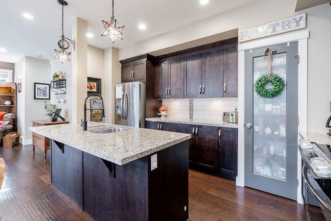 Kitchen featuring stainless steel refrigerator with ice dispenser, a sink, dark brown cabinetry, dark wood-style flooring, and recessed lighting | Image 9