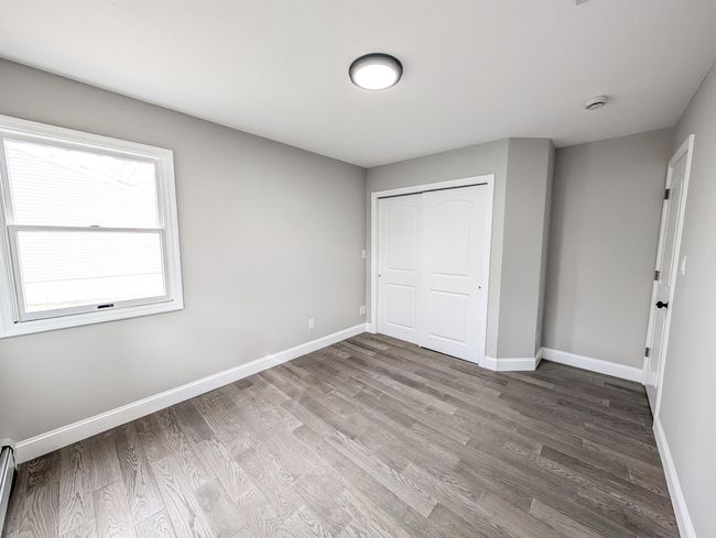 Unfurnished bedroom with baseboard heating, wood finished floors, and baseboards | Image 13