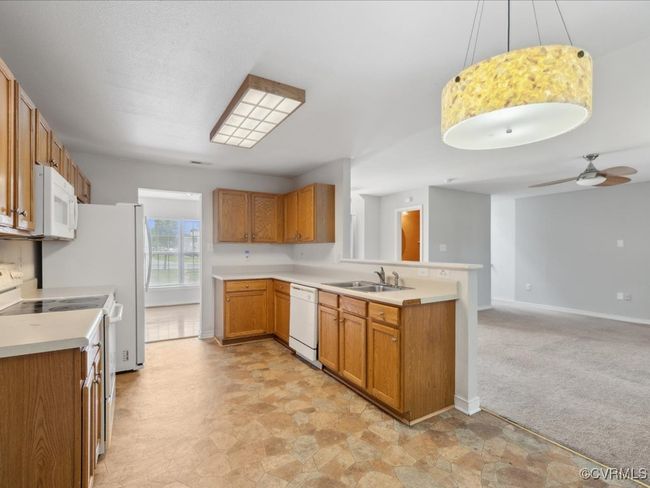 Kitchen with white appliances, a peninsula, brown cabinets, light countertops, and open floor plan | Image 15