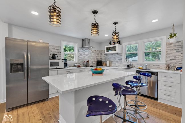 Appliances with stainless steel finishes, extractor fan, backsplash, light countertops, recessed lighting and island pendants. | Image 12