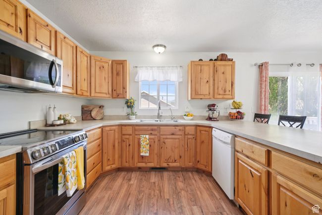 Kitchen featuring stainless steel appliances, plenty of natural light, a textured ceiling, light wood-type flooring, and light countertops | Image 9
