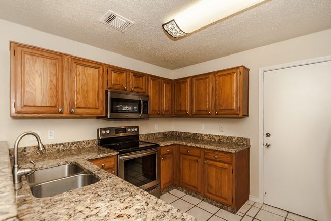 Kitchen with appliances with stainless steel finishes, light tile patterned floors, brown cabinetry, light stone countertops, and a textured ceiling | Image 7