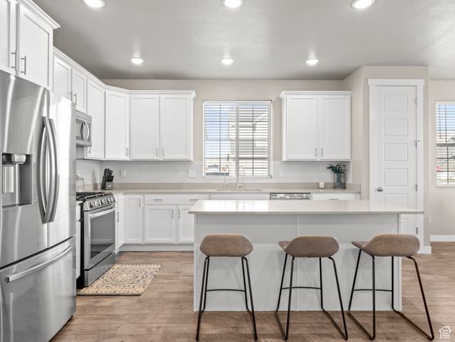 Kitchen with stainless steel appliances, a kitchen bar, white cabinets, a kitchen island, and recessed lighting | Image 11