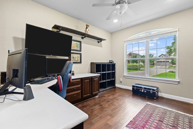 Home office with dark wood-type flooring, a ceiling fan, and baseboards | Image 20