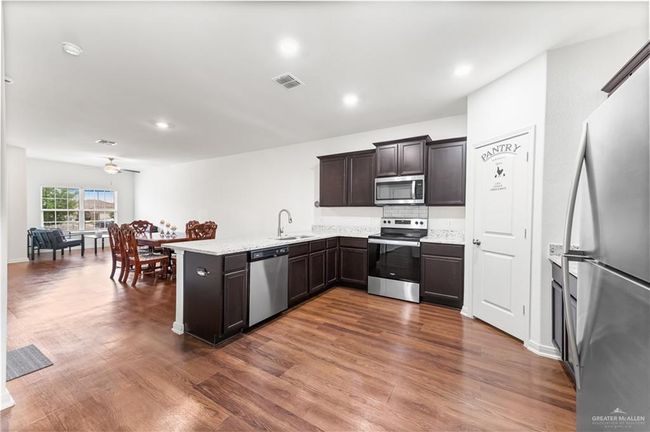 Kitchen featuring appliances with stainless steel finishes, a peninsula, dark brown cabinetry, ceiling fan, and dark wood-style floors | Image 8