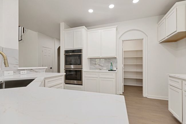 Kitchen with double oven, backsplash, light wood finished floors, white cabinetry, and recessed lighting | Image 10