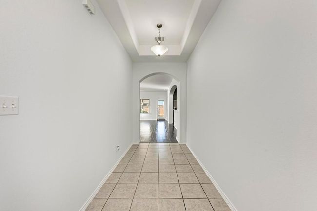 Hall with arched walkways, light tile patterned floors, baseboards, and a tray ceiling | Image 12