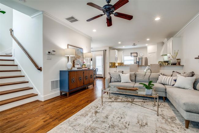 Living area with crown molding, wood finished floors, a ceiling fan, recessed lighting, and stairs | Image 5