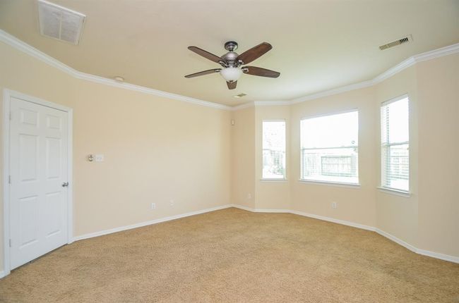 This bright primary bedroom features neutral walls, carpeted flooring, a ceiling fan, and ample natural light from three windows. Ideal for a cozy living space or bedroom. | Image 18