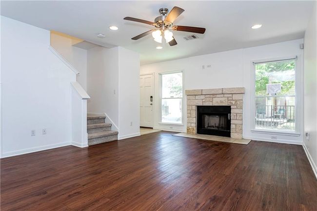 Unfurnished living room with ceiling fan, wood finished floors, stairs, a stone fireplace, and recessed lighting | Image 4