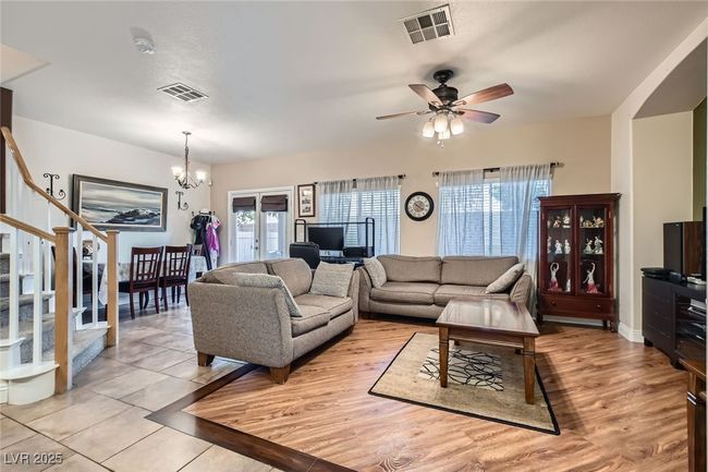 Downstairs living space (from the kitchen area) highlighting the beautiful tile and wood flooring, plenty of window lighting and other features (to include ceiling light/fan over the living room area, a dining area and partial view of the stairway). | Image 6