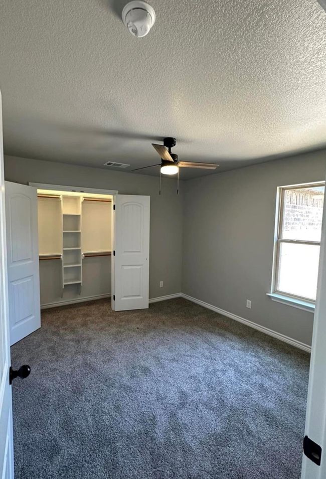 Unfurnished bedroom featuring carpet flooring, a textured ceiling, ceiling fan, and a closet | Image 10