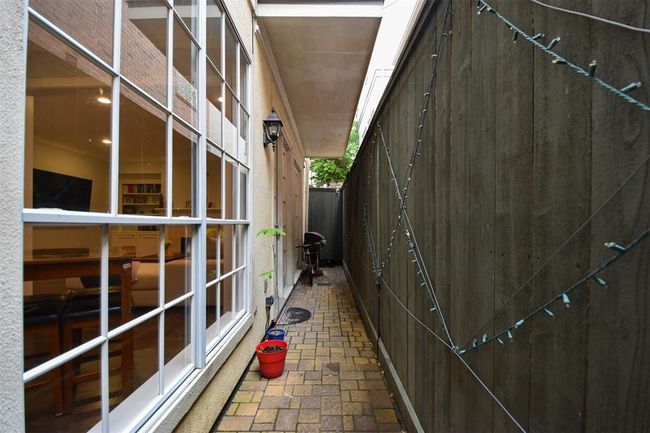 Well-lit side path of the home, featuring large windows providing a view into the family room, a secure high fence on one side, and a paved walkway offering a private access point | Image 29