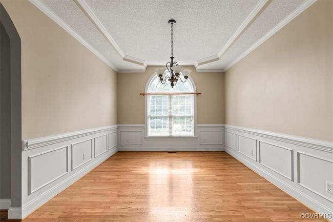 Unfurnished room with a textured ceiling, a chandelier, arched walkways, light wood finished floors, and a wainscoted wall | Image 21