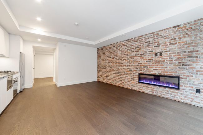 Unfurnished living room with a raised ceiling, dark wood finished floors, brick wall, recessed lighting, and a glass covered fireplace | Image 11