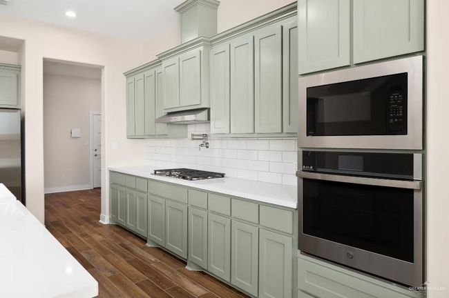 Kitchen with under cabinet range hood, dark wood-style flooring, light countertops, stainless steel appliances, and backsplash | Image 11