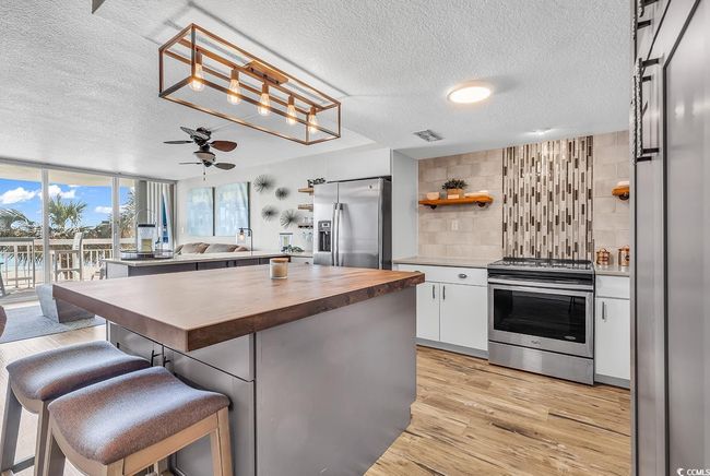 Kitchen with decorative backsplash, light wood finished floors, wood counters, appliances with stainless steel finishes, and open shelves | Image 14