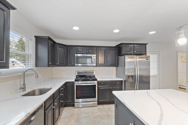 Kitchen featuring a sink, light stone countertops, decorative backsplash, and appliances with stainless steel finishes | Image 36
