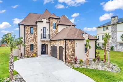 French country home featuring a balcony 3 car garage 8 car parking, stone accent, stucco siding, Palm trees, Rock Flower beds | Image 1