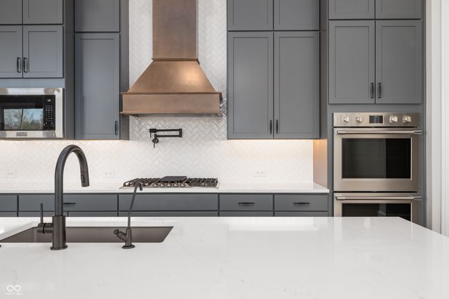 Kitchen with premium range hood, gray cabinetry, appliances with stainless steel finishes, decorative backsplash. | Image 9