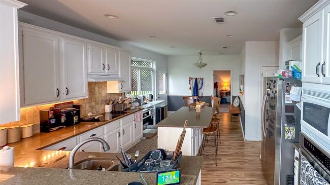 Kitchen with stainless steel appliances, light wood-type flooring, white cabinets, tasteful backsplash, and recessed lighting | Image 12