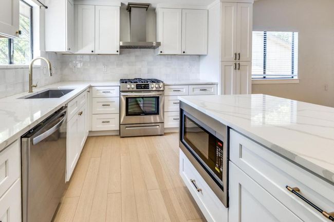 Kitchen with tasteful backsplash, stainless steel appliances, wall chimney range hood, white cabinets, and a sink | Image 14