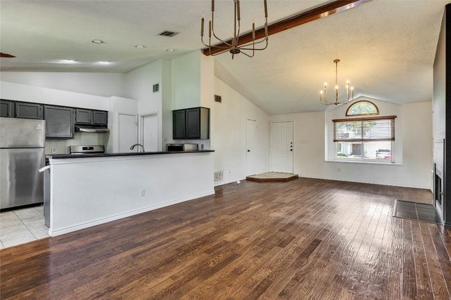 Unfurnished living room featuring wood finished floors, a fireplace with flush hearth, a chandelier, and high vaulted ceiling | Image 4