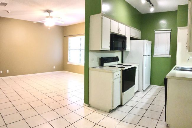 Kitchen with light countertops, a sink, black microwave, white range with electric cooktop, and light tile patterned floors | Image 6