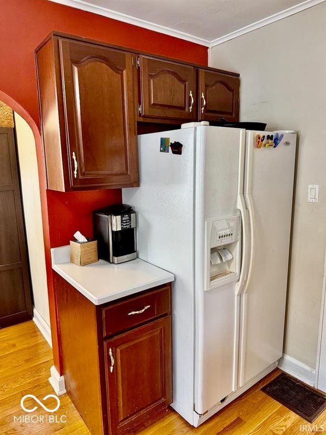 kitchen with white refrigerator with ice dispenser, light countertops, light wood-style flooring, arched walkways, and crown molding | Image 23
