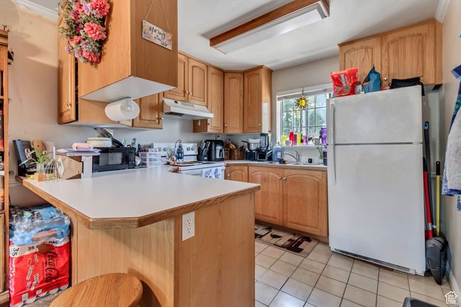 Kitchen with white appliances, under cabinet range hood, a peninsula, light tile patterned floors, and light countertops | Image 8