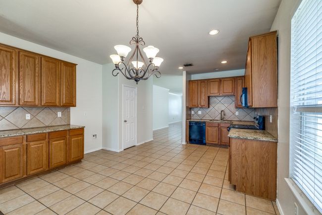 Kitchen featuring brown cabinets, light tile patterned floors, an inviting chandelier, and dishwasher | Image 7